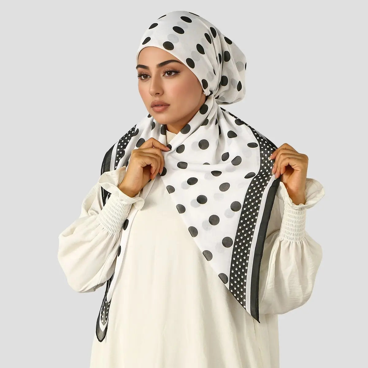 Eine Frau trägt ein weißes Oberteil und einen schwarzen Polka-Dot-Hijab mit schwarzem Rand.