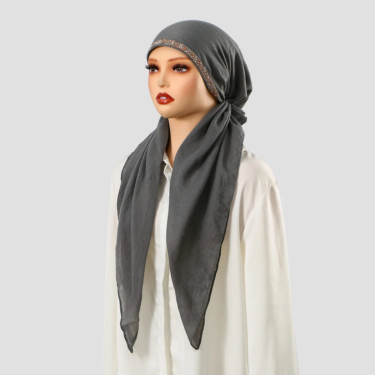 Une femme portant un bonnet hijab en lin gris uni avec broderie dorée et un haut blanc.