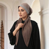 Eine Frau trägt einen braunen Stoff-Hijab mit einem silbernen Diamant-besetzten Band und einem schwarzen Oberteil.