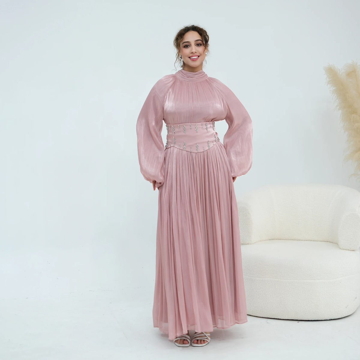Une femme modélise une abaya rose poudré avec un tissu texturé et une ceinture ornée.