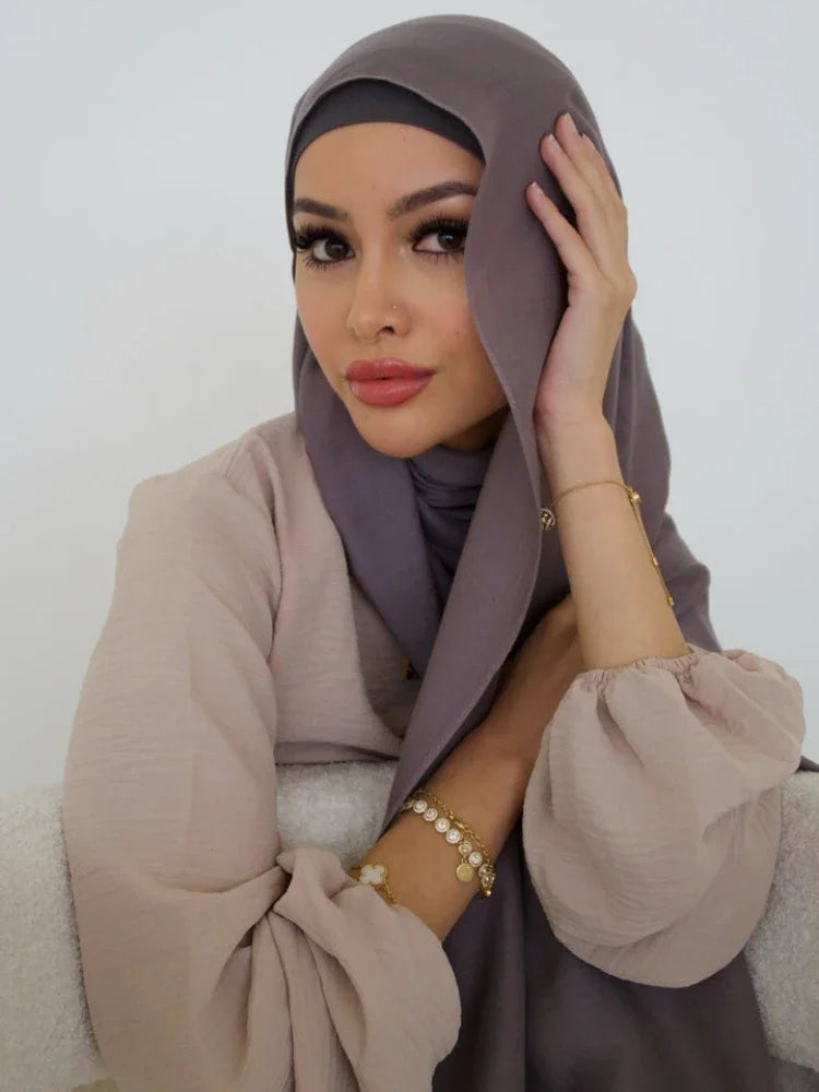 A woman wearing a soft mauve hijab and matching top, posing indoors.