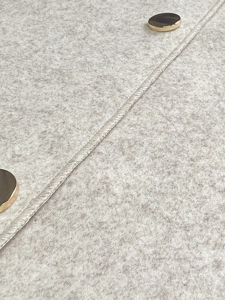 Gros plan sur un tissu en laine gris clair avec une couture visible et deux boutons ronds dorés.