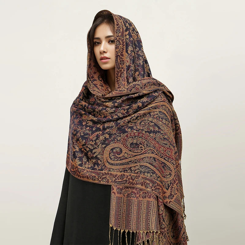 Una mujer modela un pañuelo pashmina de lujo con patrón marrón oscuro y dorado sobre su cabeza.