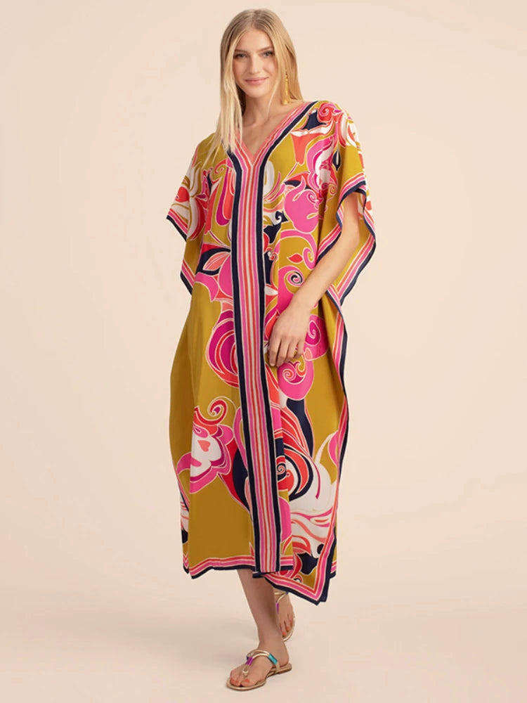 Una mujer modela un vestido caftán playero amarillo con estampado floral rosa y morado vibrante.