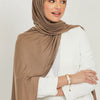 Eine Frau trägt einen einfarbigen braunen Jersey-Hijab und einen weißen Blazer.