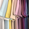 Un présentoir d'abayas simples dans diverses teintes pastel et joyaux profonds, accrochées pour exposition.