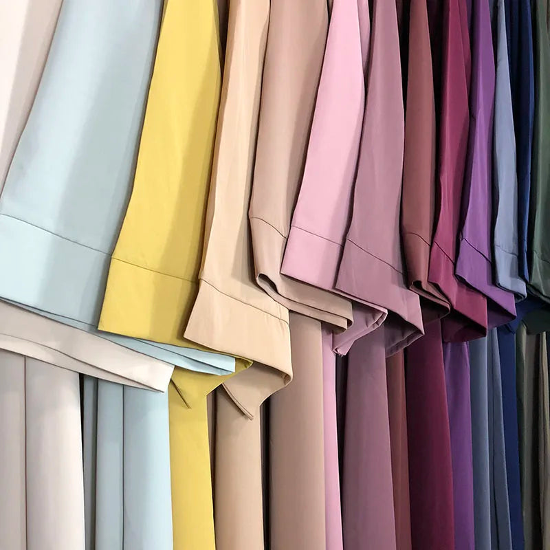 Un présentoir d'abayas simples dans diverses teintes pastel et joyaux profonds, accrochées pour exposition.