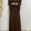 Eine Frau trägt ein fließendes, offenes braunes Abaya-Kaftan mit einem weißen Untergewand.