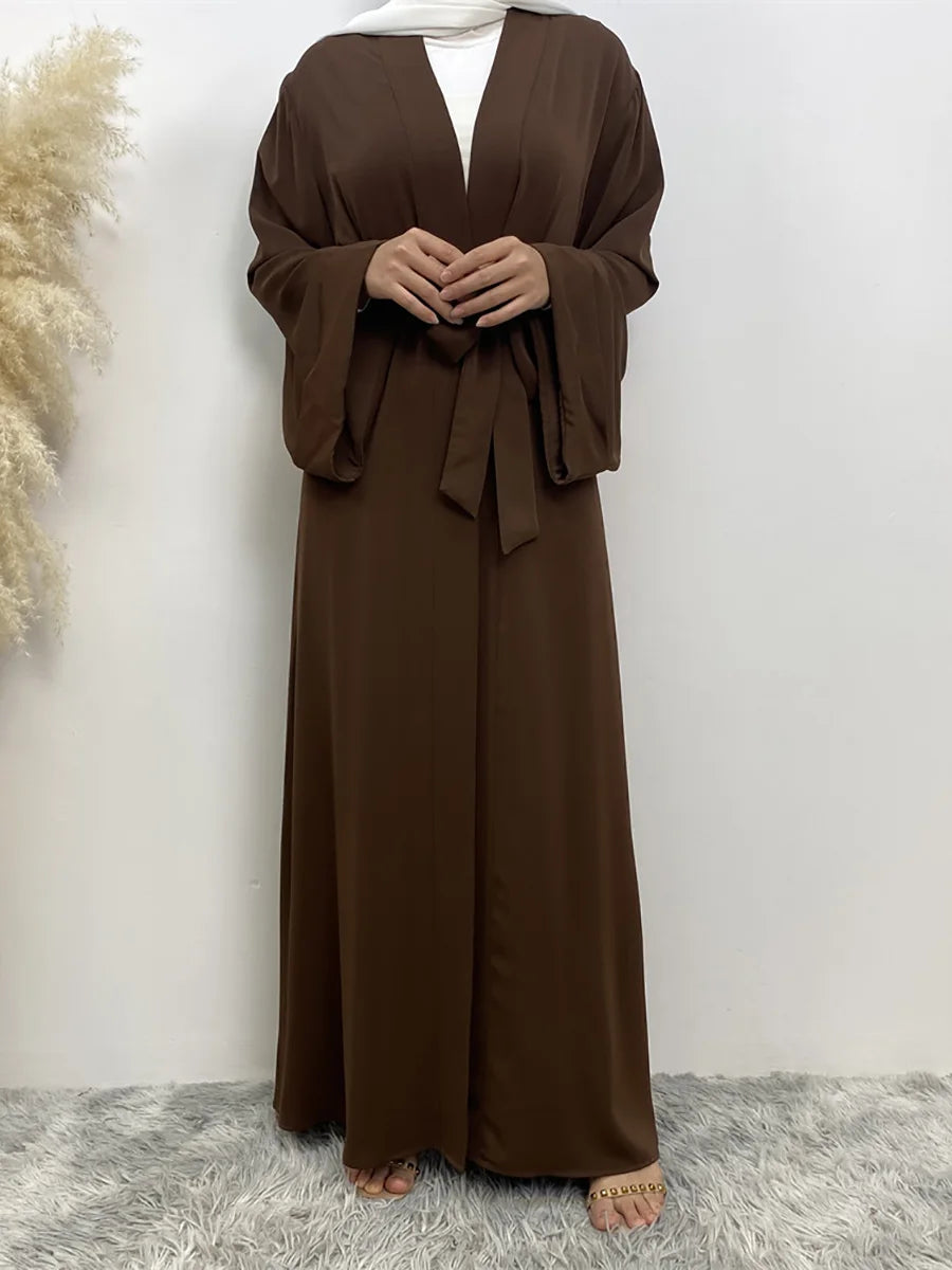 Eine Frau trägt ein fließendes, offenes braunes Abaya-Kaftan mit einem weißen Untergewand.