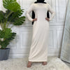Ein langes beige Maxi-Abaya-Kleid mit langen Ärmeln und einem schwarzen Hijab, präsentiert vor einer weißen Wand.