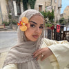 Une femme portant un foulard chiffon beige avec bordure de dentelle à cils, regardant directement l'appareil photo.