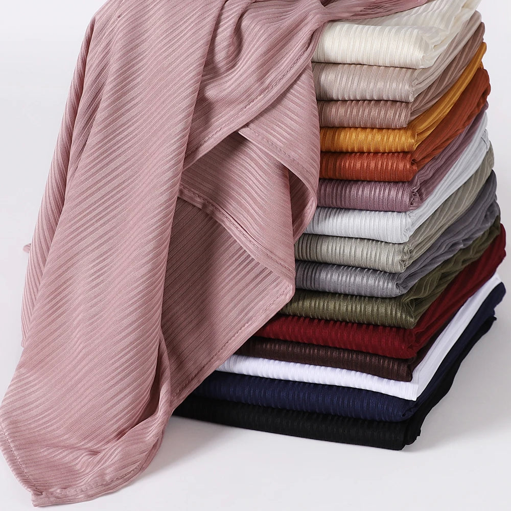 A stack of ribbed jersey hijab scarves in various shades of pink, brown, olive green, and gray.