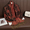 Pañuelo pashmina de lujo con patrón marrón y rojo drapeado sobre una superficie de cuero marrón.