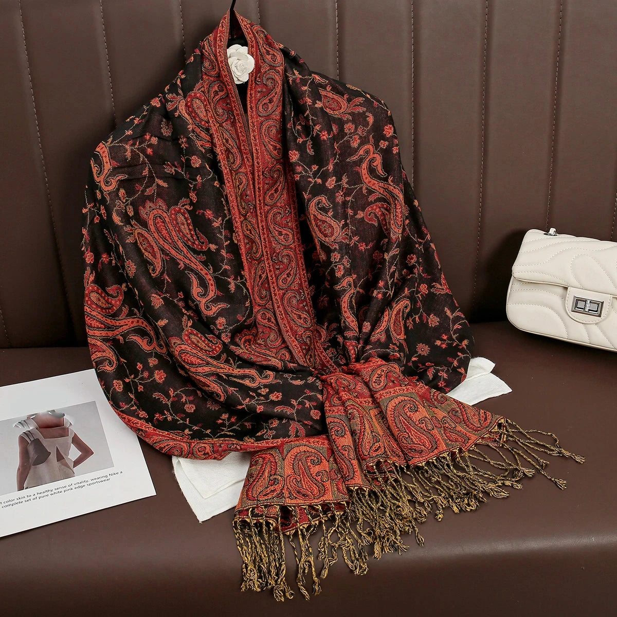Pañuelo pashmina de lujo con patrón marrón y rojo drapeado sobre una superficie de cuero marrón.