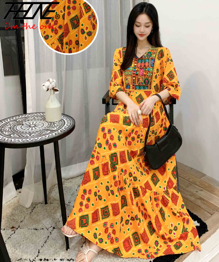 Eine Frau modelliert ein leuchtend orange, bohemienhaft besticktes Maxi-Kleid mit Blumenmustern.