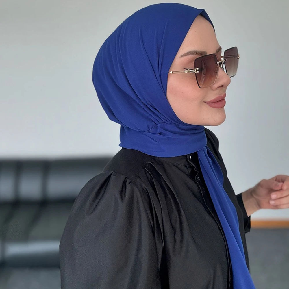 Una mujer vistiendo un hiyab instantáneo azul real y gafas de sol, mirando hacia un lado.