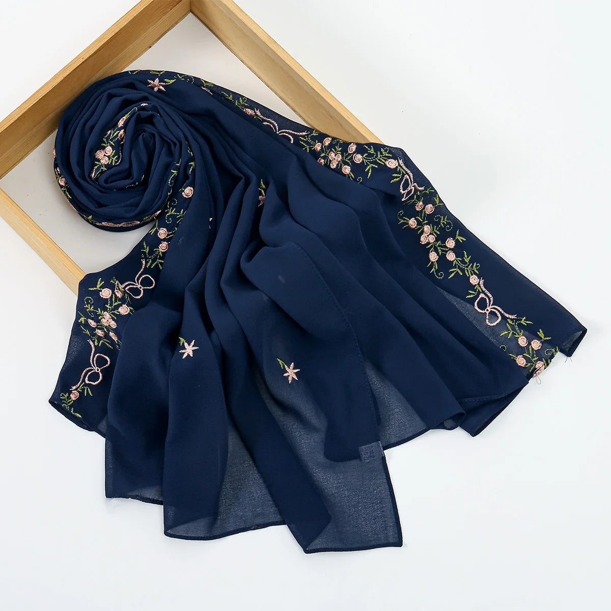 A dark navy blue chiffon hijab shawl with delicate floral embroidery, displayed on a wooden frame.