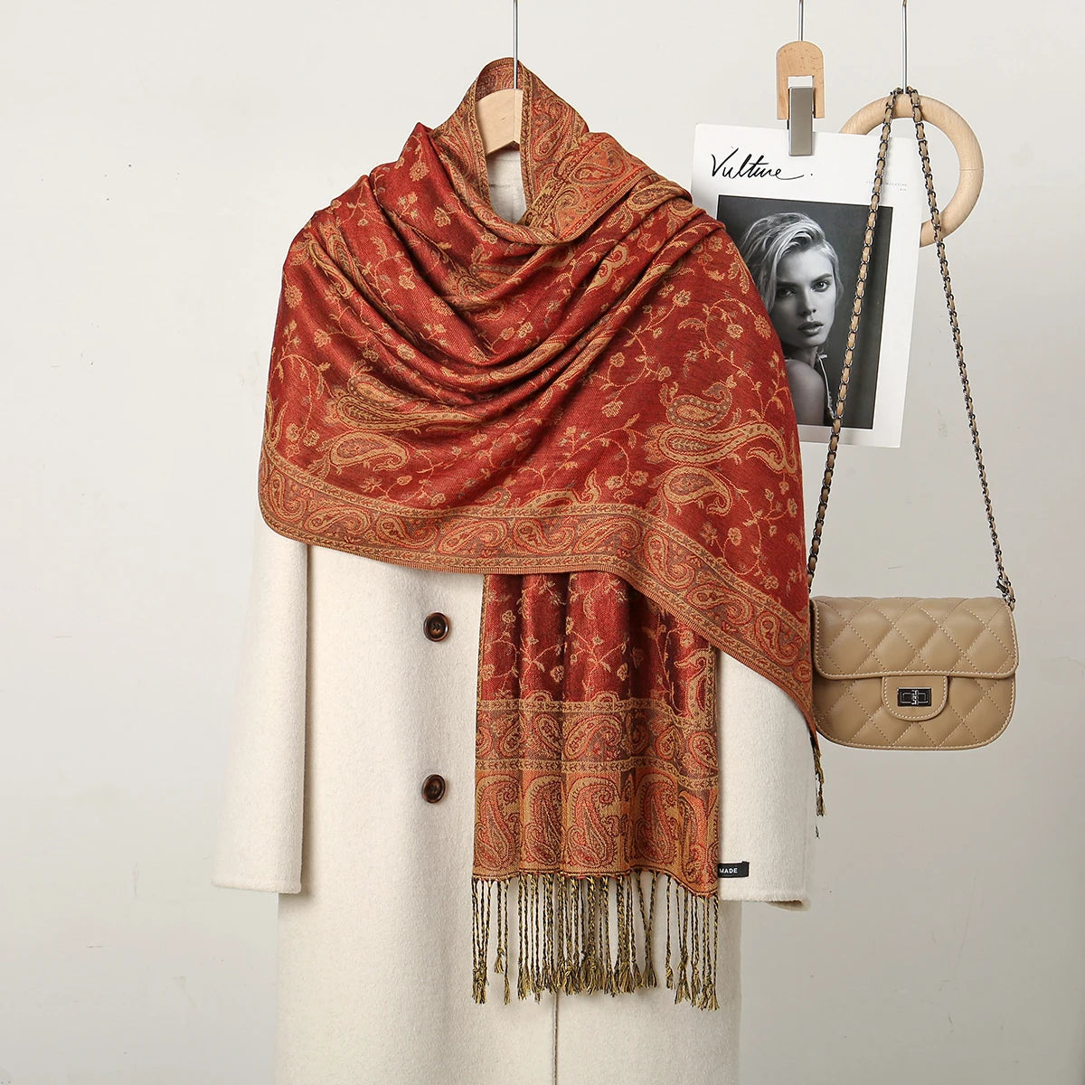 Chal vintage de bordado paisley naranja rojizo colgado en un percha blanca.