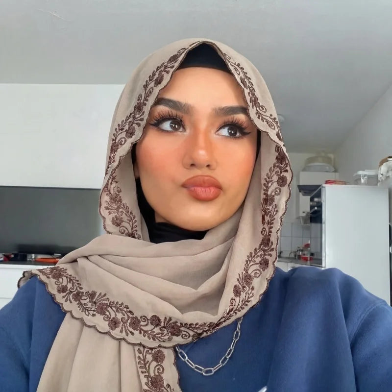 Une femme portant un foulard de chiffon beige avec une bordure en dentelle marron et un haut bleu foncé.