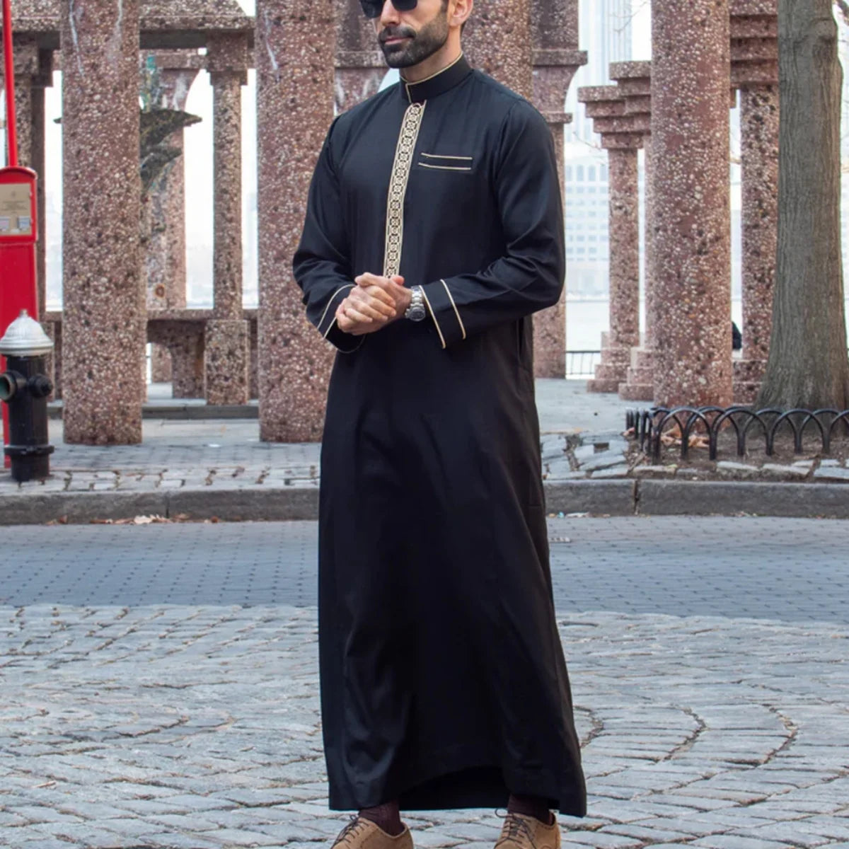 Mann in schwarzem besticktem Langarm-Arabischer Thobe im Freien stehend.