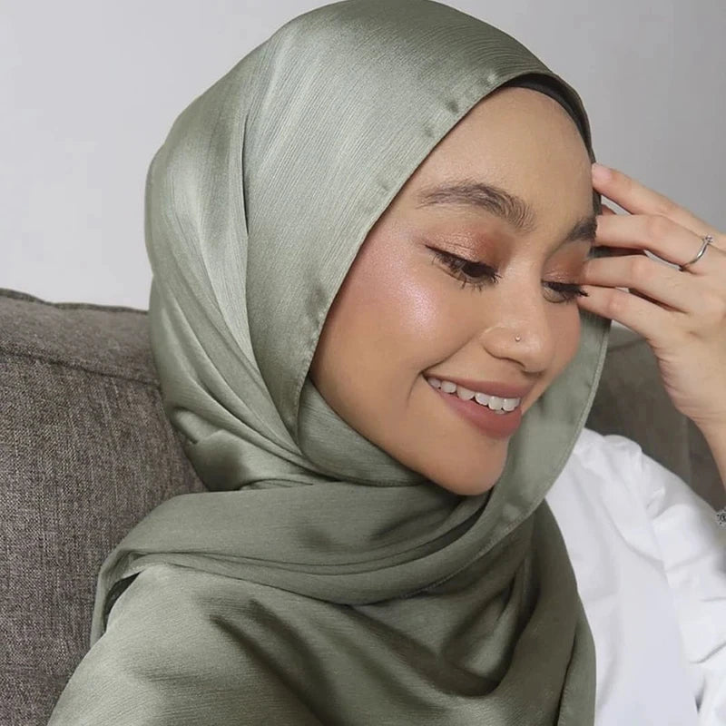 Eine Frau trägt einen salbeigrün-satinierten, gekräuselten Hijab-Schal und lächelt nach unten.