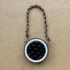 Collar de cadena plateada con dije circular acolchado negro sobre papel marrón.