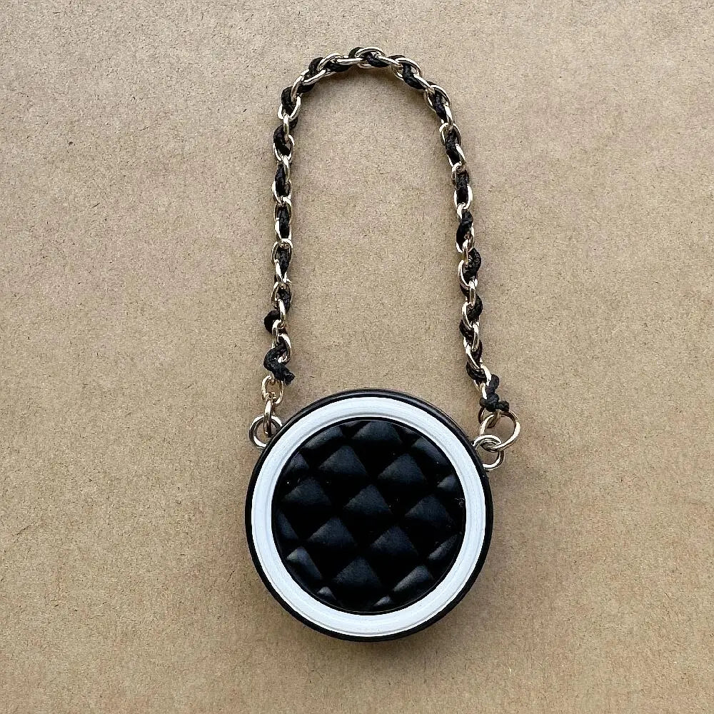 Collar de cadena plateada con dije circular acolchado negro sobre papel marrón.