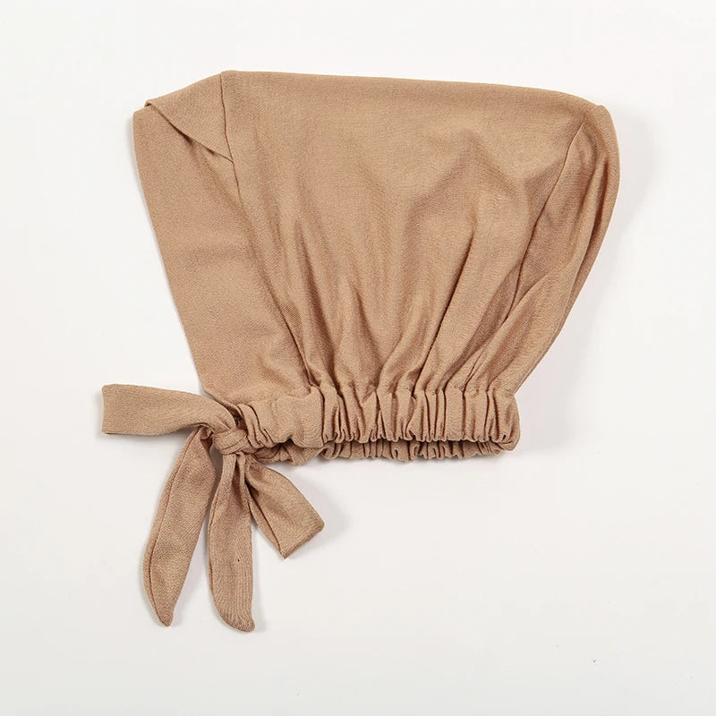 A beige adjustable cotton jersey inner hijab cap folded and tied with a fabric tie.