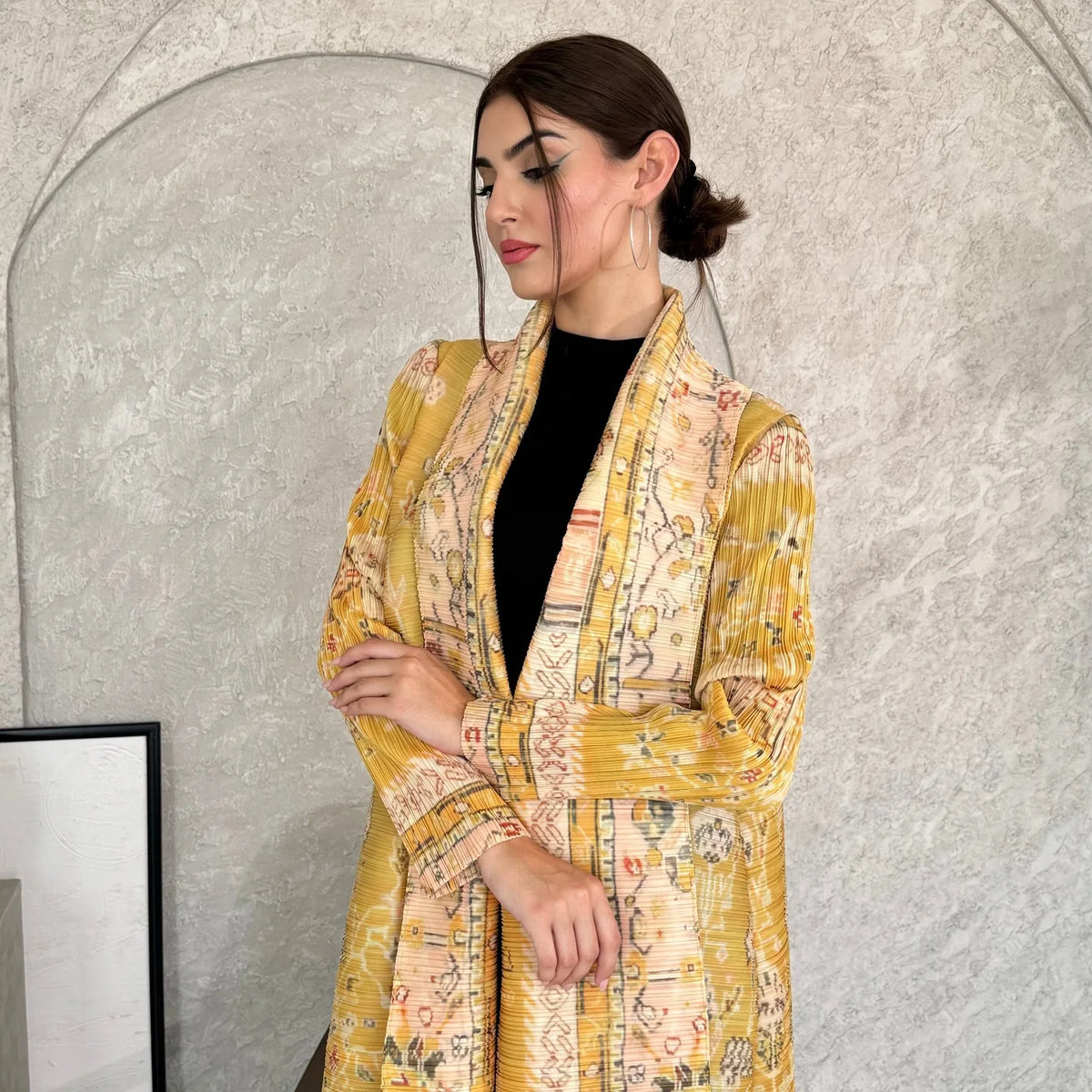 Eine Frau trägt einen fließenden, plissierten Abaya-Cardigan in Gelb und Beige mit Stickereien über einem schwarzen Top.
