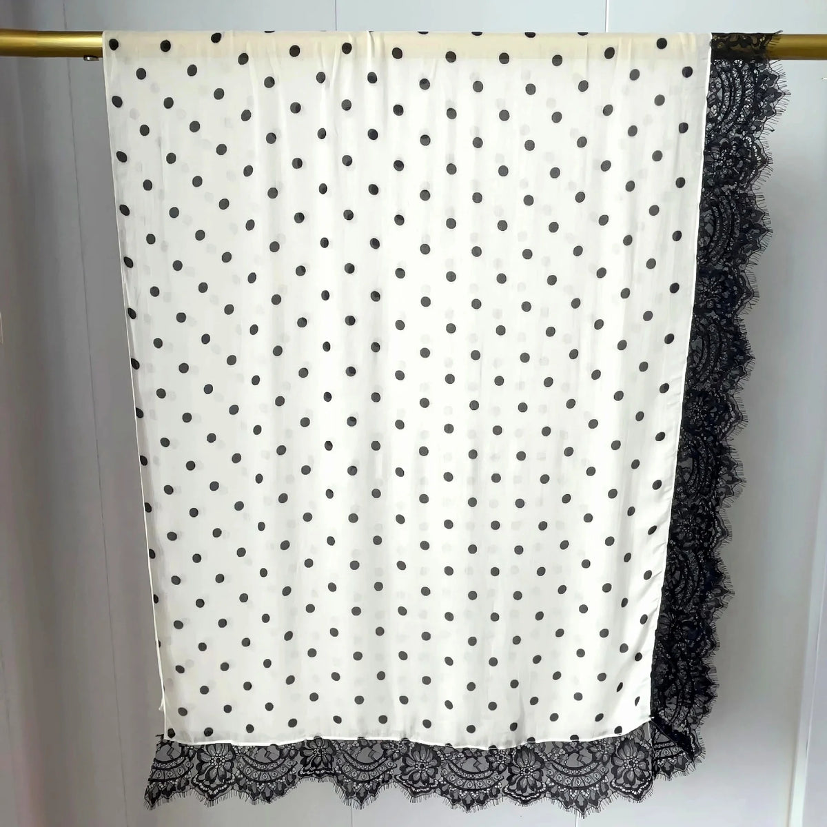 Hijab de tela blanca con puntos negros colgado en una barra.