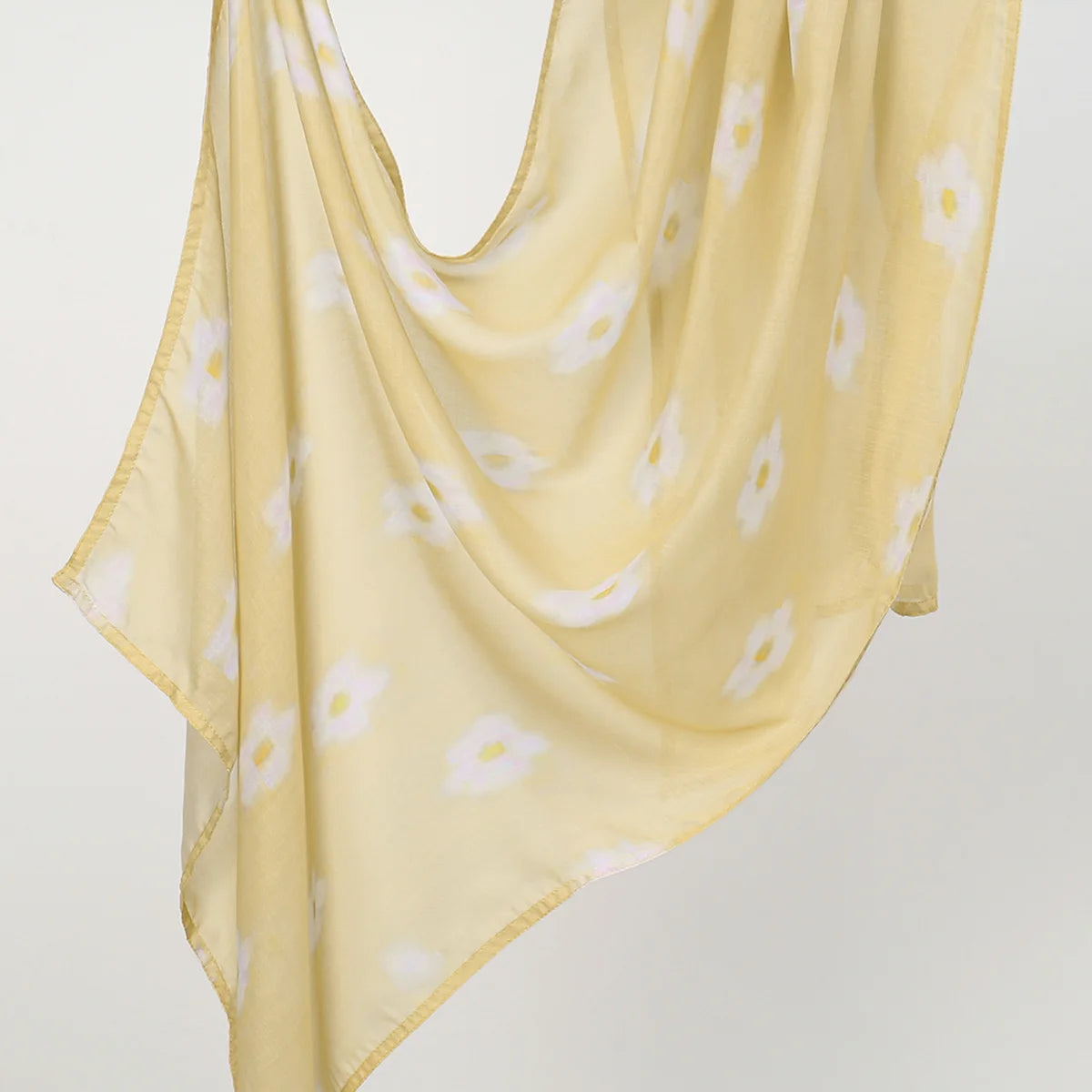 Helles gelbes, durchscheinendes Hijab-Schal mit weißem Blumenmuster, sanft drapiert.