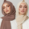 Modelin trägt einen braunen Chiffon-Hijab und ein weißes Oberteil und blickt direkt in die Kamera.