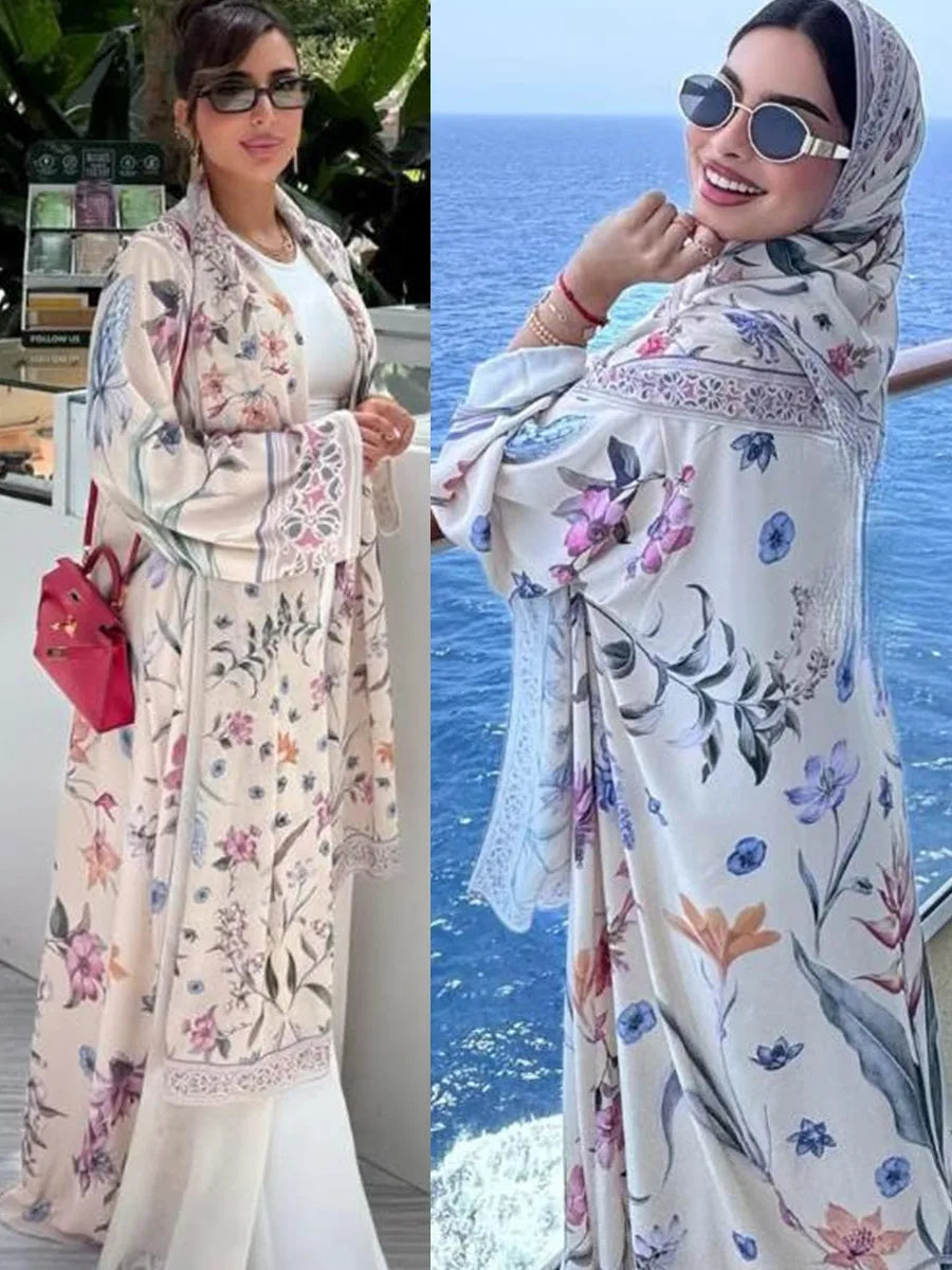 Una mujer modela un vestido kaftan largo de estampado floral en rosa claro y blanco contra un fondo de mar azul.