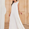A woman models a white flowing modest abaya dress with long sleeves and a high slit in an indoor setting.