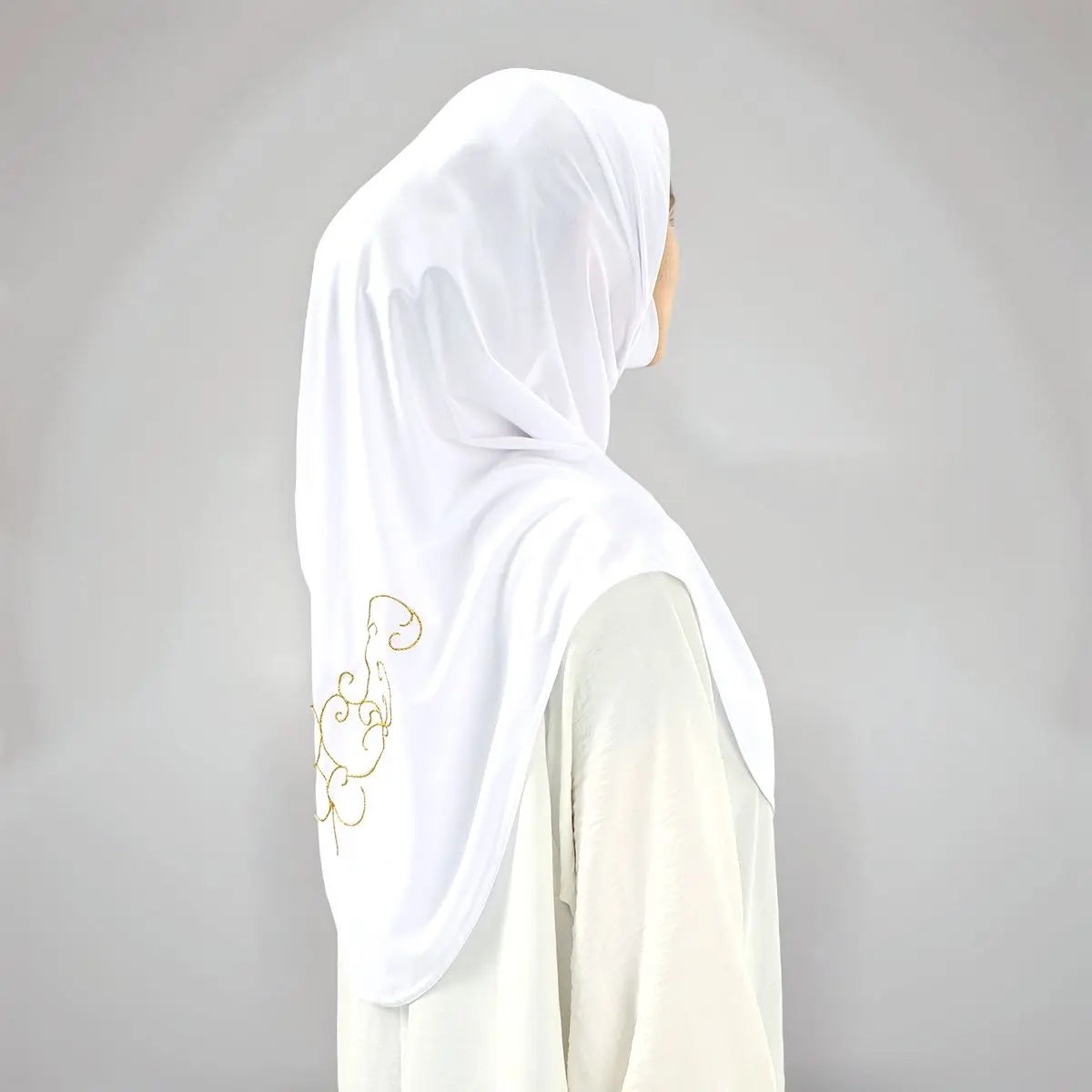 Hijab blanc avec broderies dorées porté sur un vêtement de couleur claire.