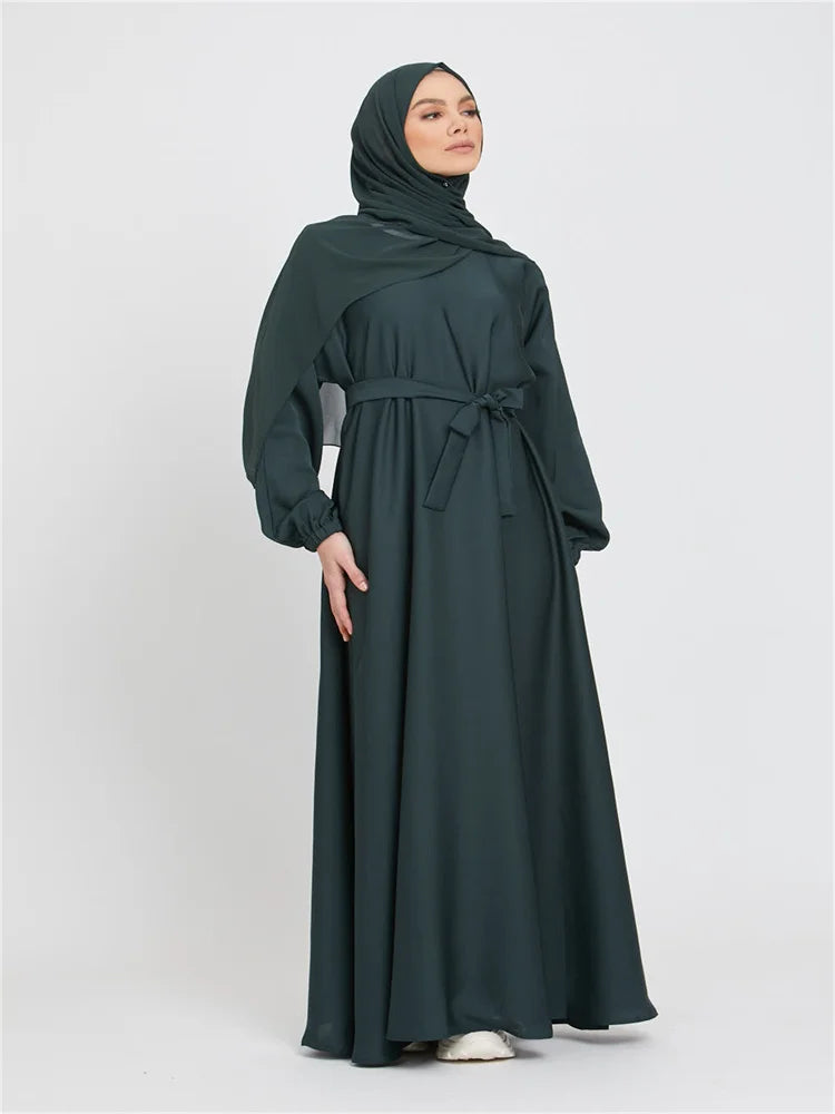 Eine Frau trägt eine dunkelgrüne marokkanische Kaftan-Abaya mit Hijab und gebundener Taille.