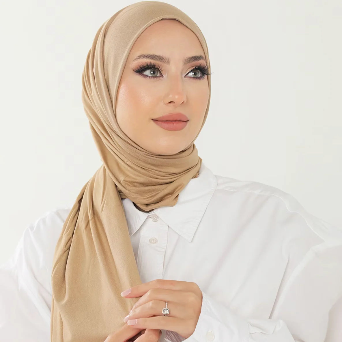 Una mujer vistiendo un pañuelo de hijab de algodón premium y elástico beige y una camisa blanca.