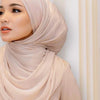 Primer plano de una mujer vistiendo un chal de hijab de gasa plisada y brillante color beige.