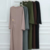 Abaya beige à cordon de serrage suspendue sur un cintre en bois contre un mur blanc.