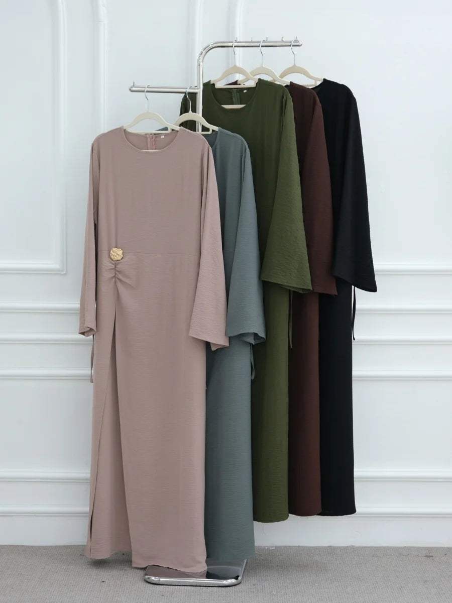 Abaya beige à cordon de serrage suspendue sur un cintre en bois contre un mur blanc.