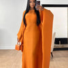 Una mujer modela un vestido abaya de satén naranja con vuelo en un estudio.