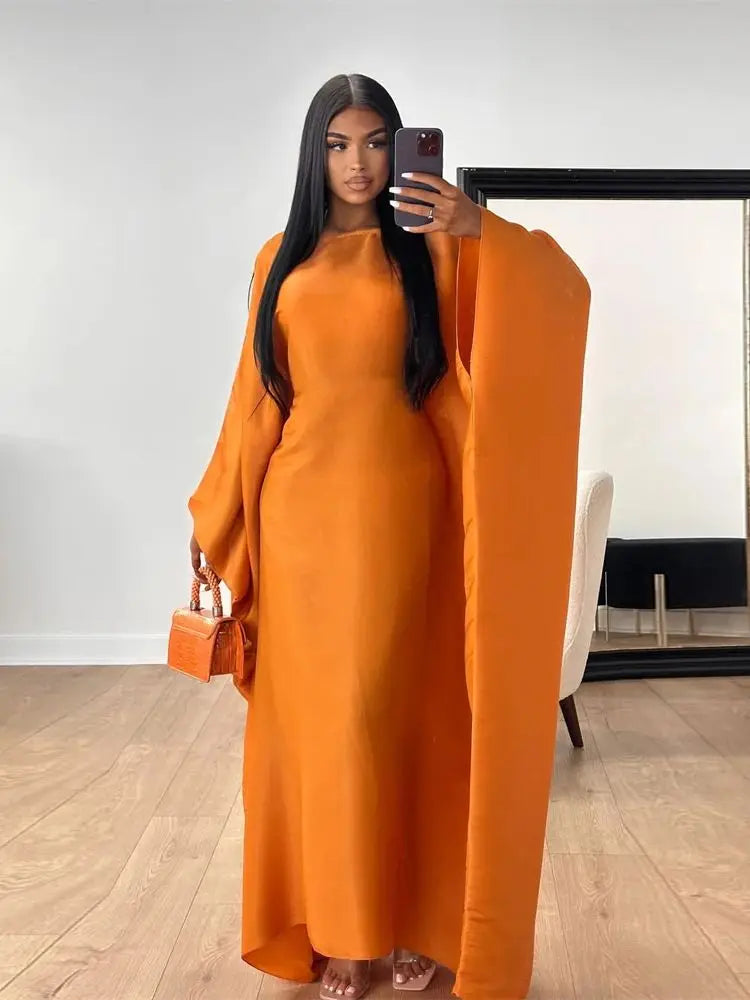 Una mujer modela un vestido abaya de satén naranja con vuelo en un estudio.