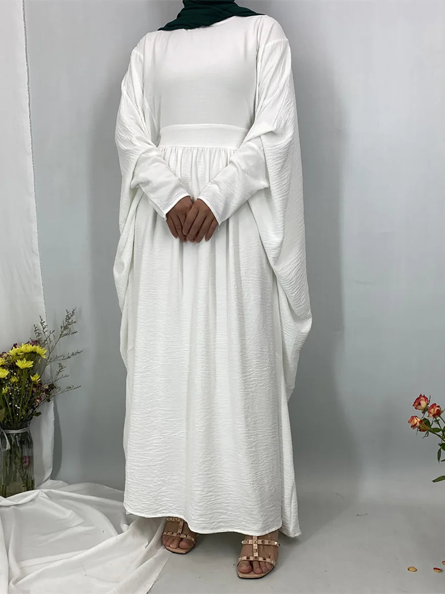 Eine Frau in einem eleganten weißen Batwing-Abaya mit schwarzem Hijab vor einem hellgrauen Hintergrund.