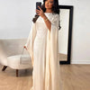 Una mujer modela una abaya satinada color crema en forma de ala mientras se toma una selfie en una habitación brillante.