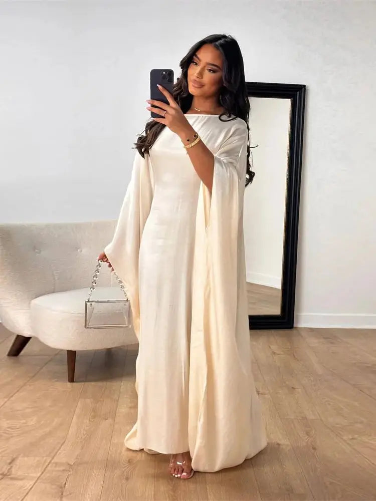 Una mujer modela una abaya satinada color crema en forma de ala mientras se toma una selfie en una habitación brillante.