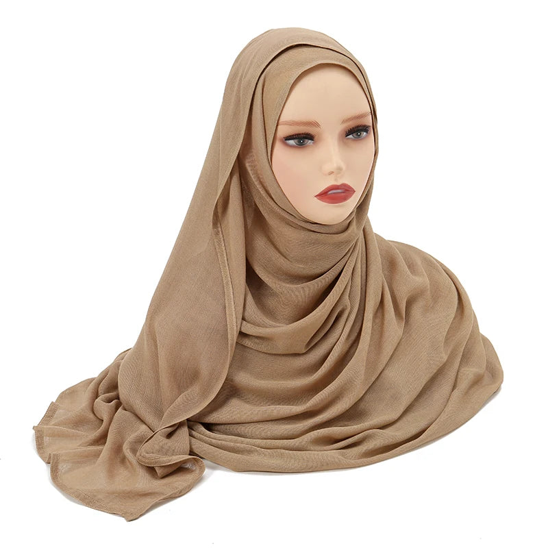 Una modelo vistiendo un chal hijab de algodón rayón beige, drapeado alrededor de la cabeza y el cuello.