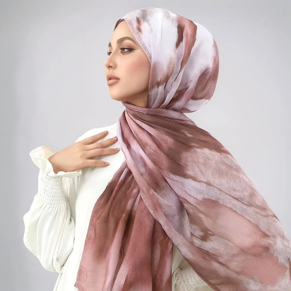 A woman wearing a watercolor print cotton linen hijab scarf in shades of dusty rose and beige.