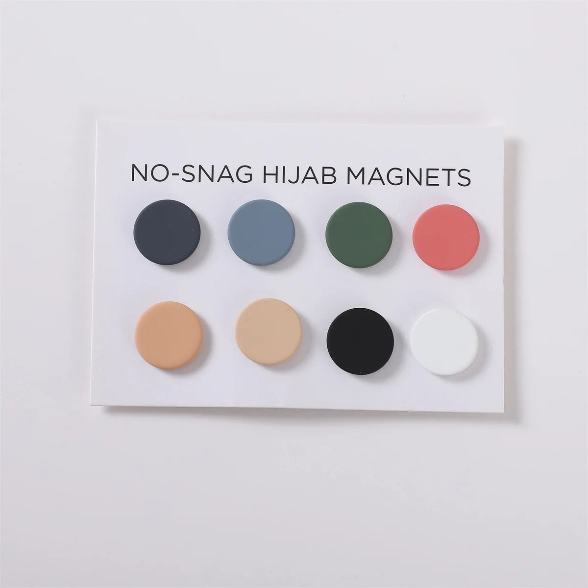 Tarjeta blanca con seis pines magnéticos redondos de hijab en varios colores como negro, azul-gris, verde oliva, coral y beig