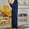 Una persona vistiendo una caftán de abaya islámica larga y azul oscuro, de pie en un elegante interior.