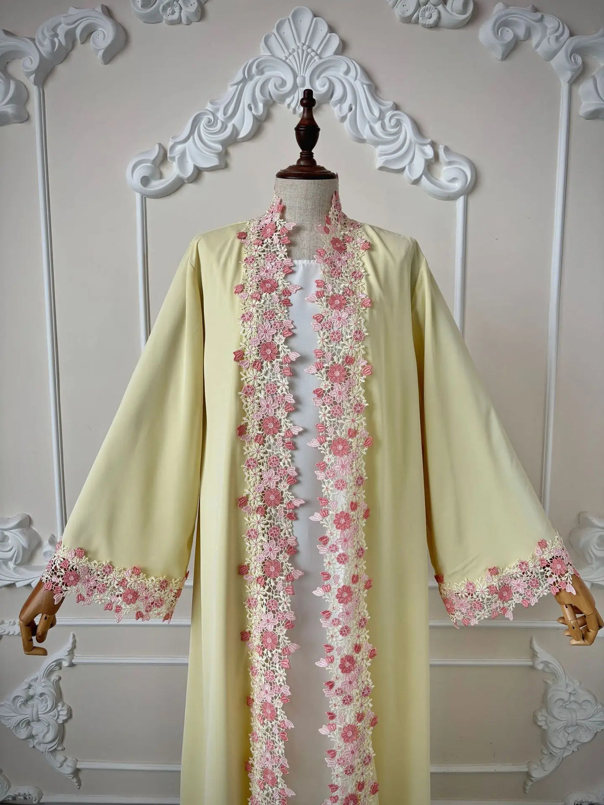 Une longue abaya jaune pâle avec des bordures de dentelle florale rose délicates sur le col avant.
